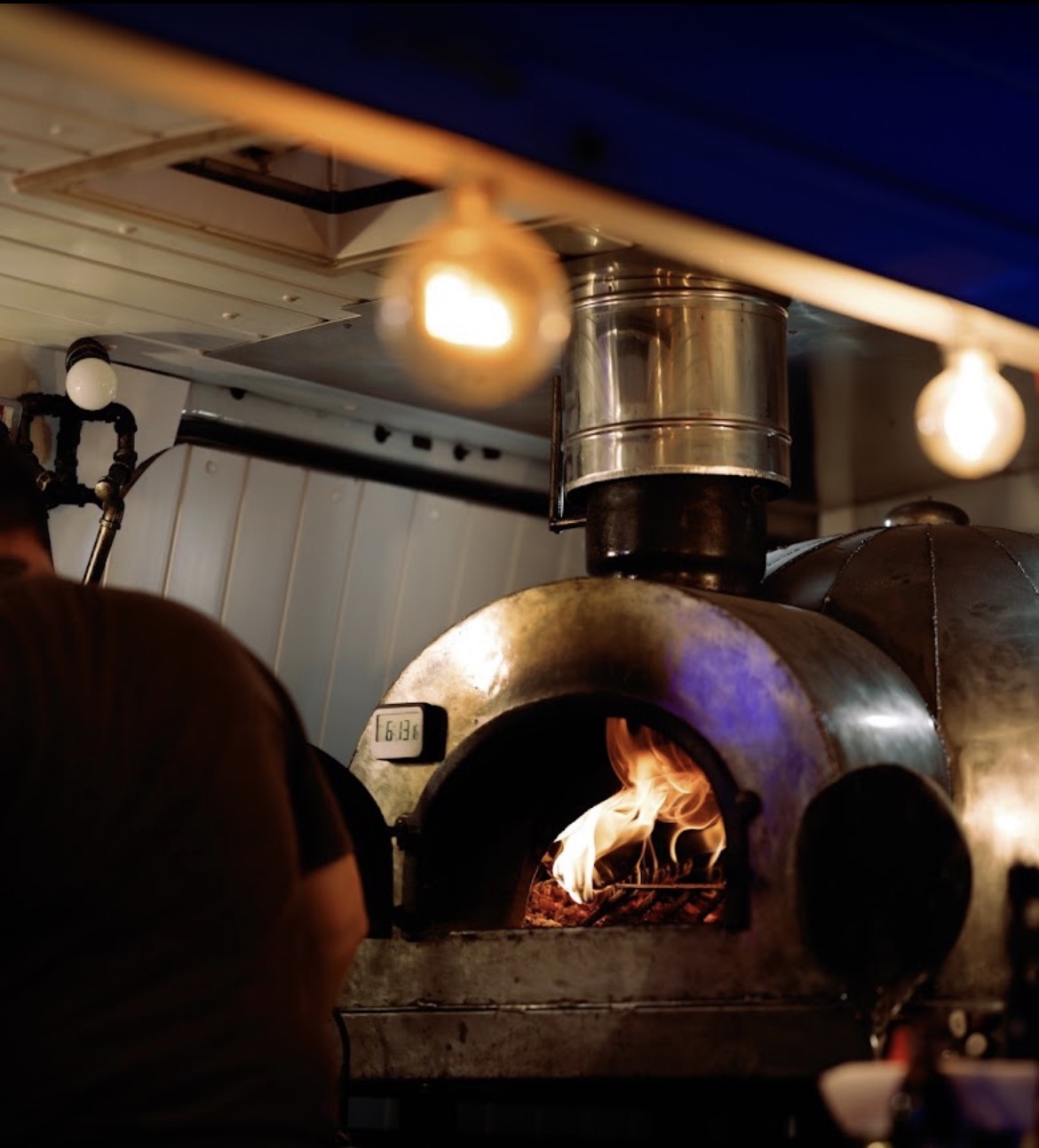 Wood-fired pizza oven with roaring flames inside the Taste of Naples mobile kitchen
